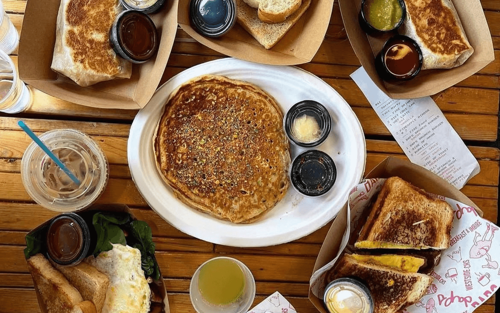 A wooden table spread with pancakes, burritos, and sandwiches at a breakfast spot in Downtown Charleston, SC
