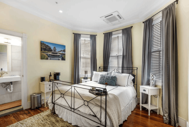 Bright B&B bedroom with black wrought iron bed, yellow walls, grey curtains, and large windows.