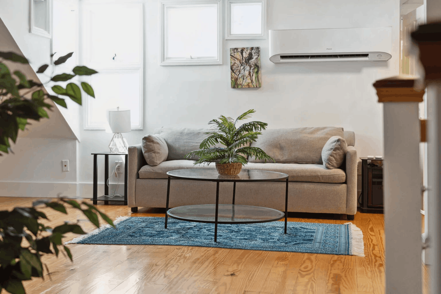 Inside a beautifully styled living suite at 257 Rutledge in downtown Charleston, SC, showcasing a cozy beige sofa, vintage blue area rug, and modern ductless AC unit.