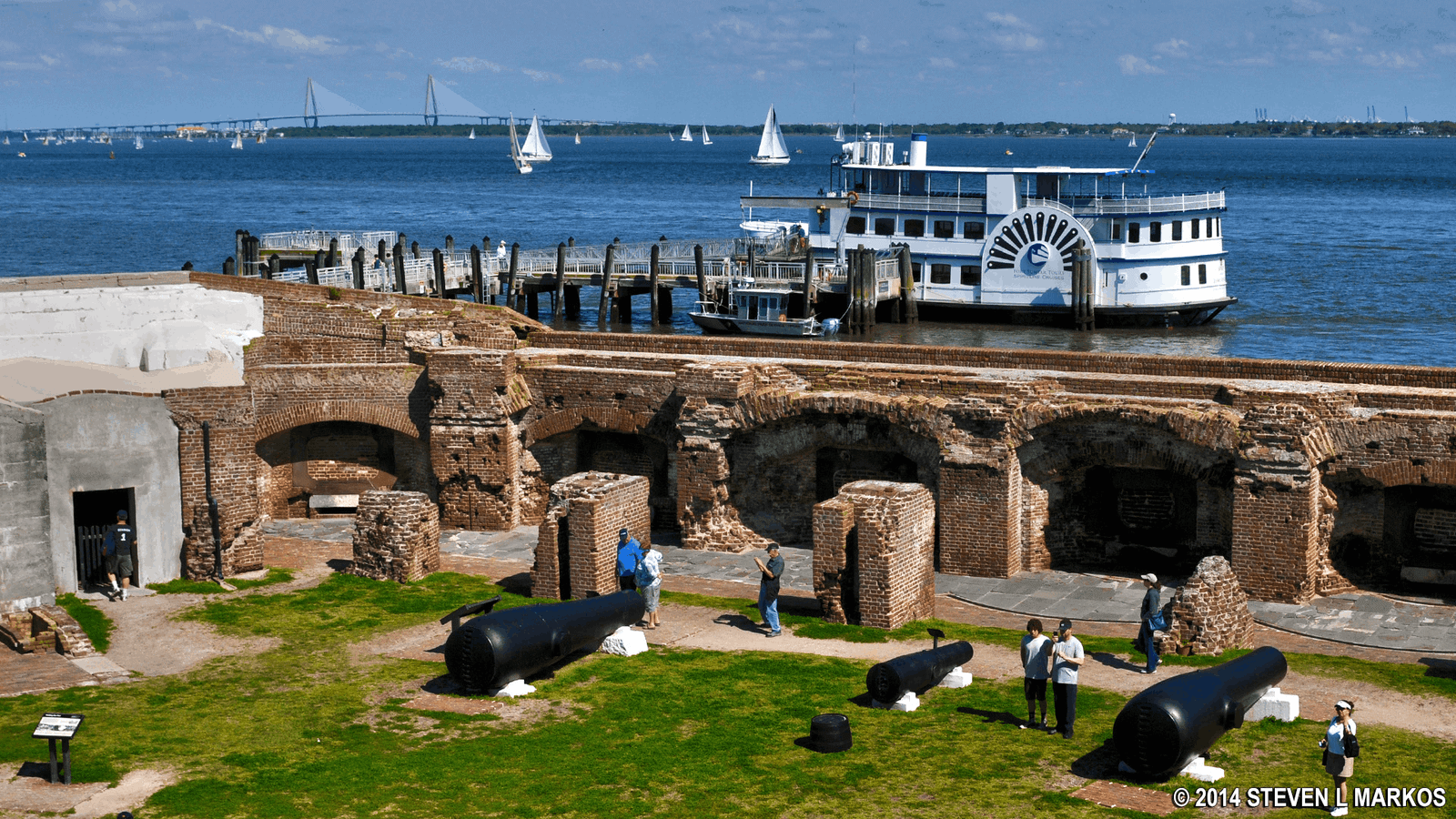 Tourists exploring the historic brick ruins and historic cannons inside Fort Sumter National Monument in Charleston Harbor, South Carolina, with a tour boat docked at the pier.