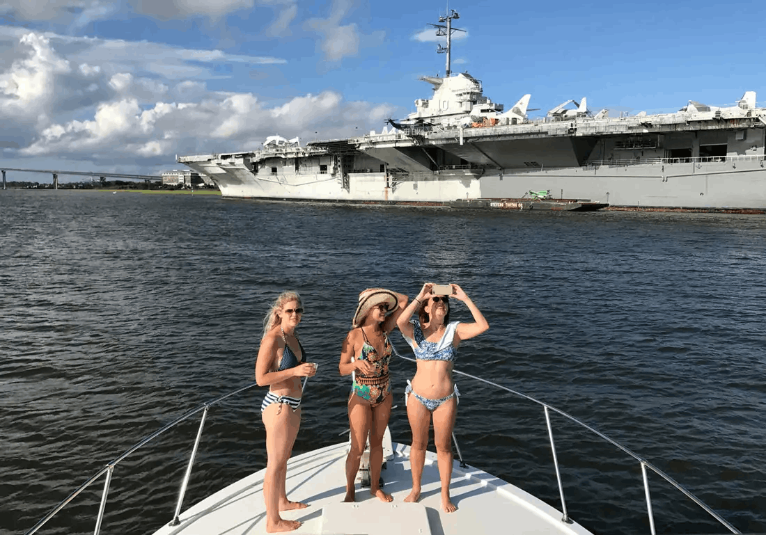 Tourists on a private boat tour taking photos of the historic USS Yorktown aircraft carrier in Charleston Harbor.