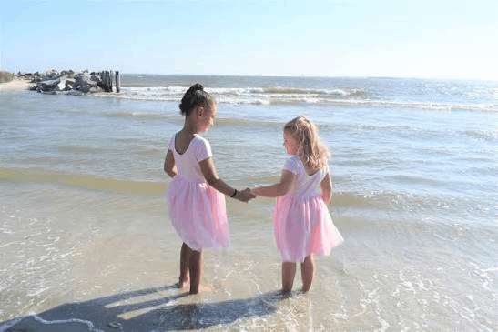 Two young girls in pink dresses holding hands while standing in the ocean water at Sullivan's Island beach near Charleston
